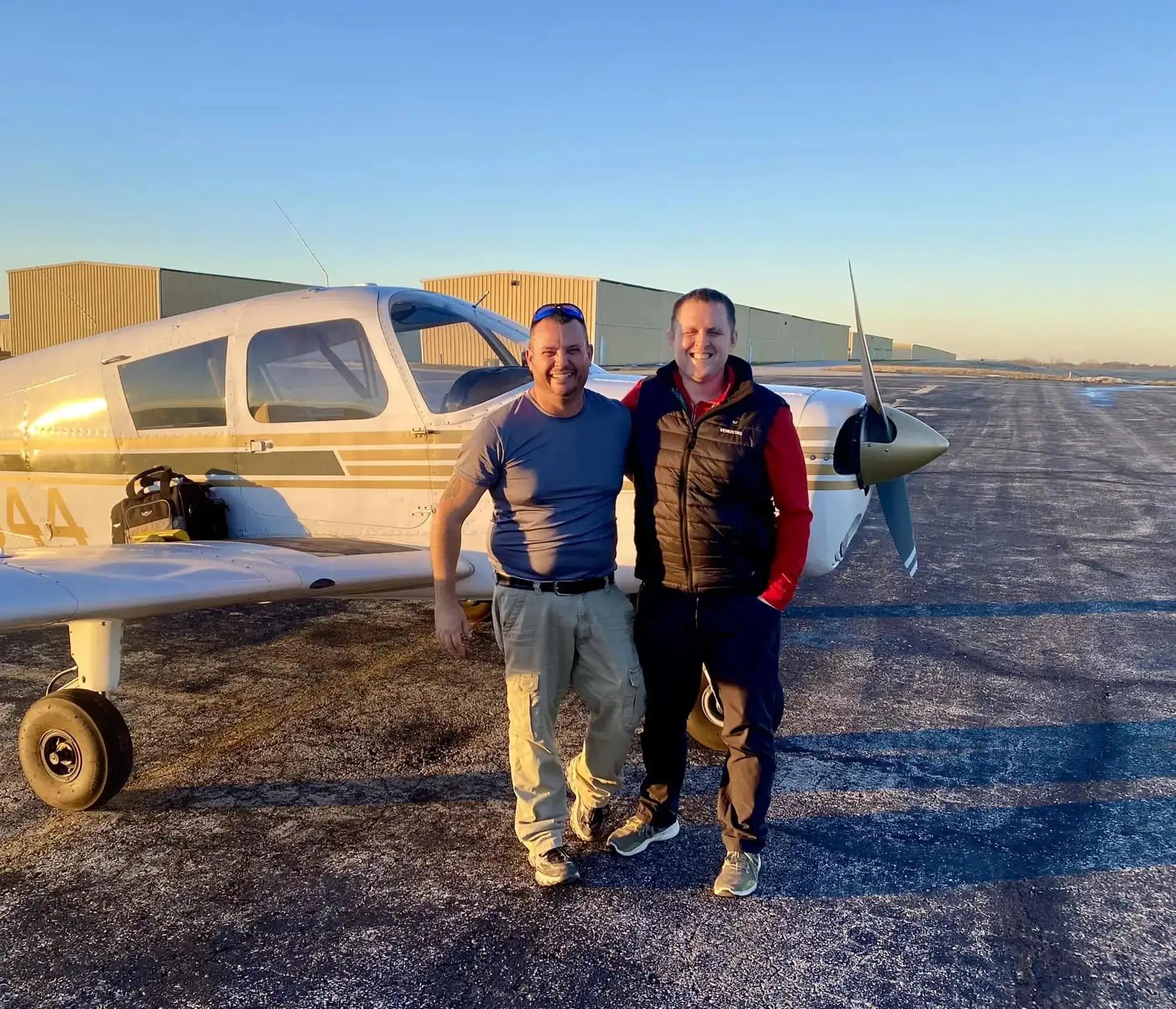 Student pilot and CFI standing side by side in front of a plane at sunset