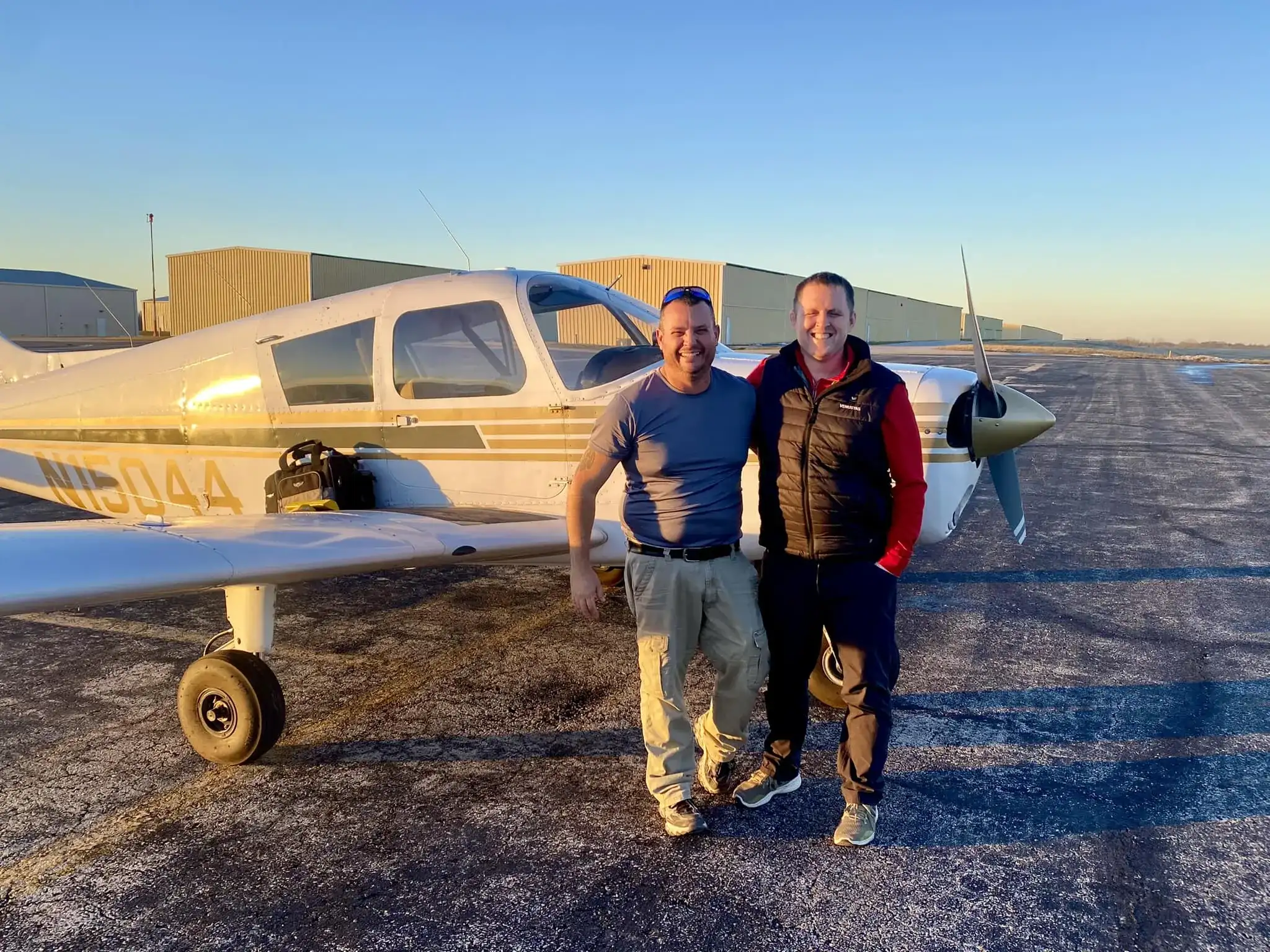 Student pilot and CFI standing side by side in front of a plane at sunset