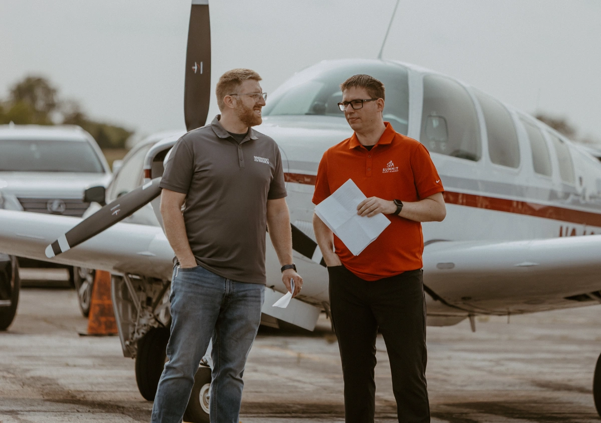Summit Flight Academy's new hangar groundbreaking ceremony at Lee's Summit Airport, featuring a group of people with shovels and aircraft in the background.