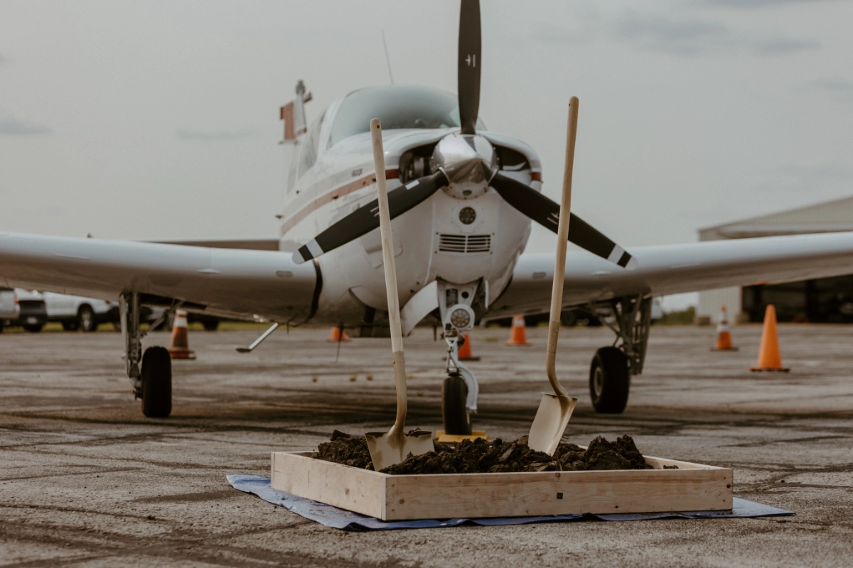 Summit Flight Academy's new hangar groundbreaking ceremony at Lee's Summit Airport, featuring a group of people with shovels and aircraft in the background.
