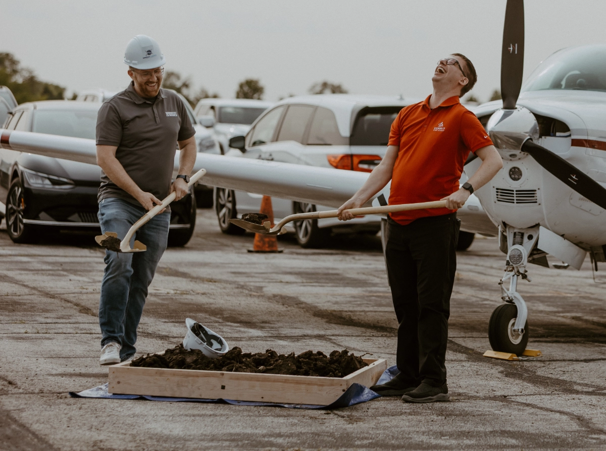 Summit Flight Academy's new hangar groundbreaking ceremony at Lee's Summit Airport, featuring a group of people with shovels and aircraft in the background.