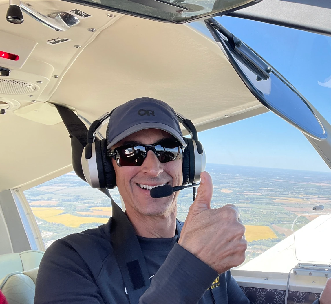 Pilot in the cockpit flying the plane while smiling and giving a thumbs up to the camera